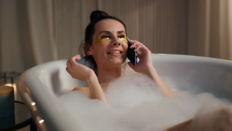 Bath-girl-calling-mobile-phone-laying-foam-water-at-home.-Smiling-lady-talking