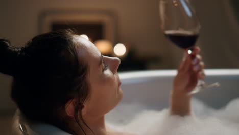 Sensual-model-sipping-wine-glass-resting-bathroom.-Woman-touching-skin-chilling