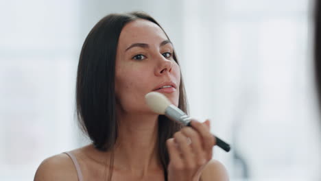 Focused-girl-powdering-face-using-brush-at-home-closeup.-Woman-applying-makeup
