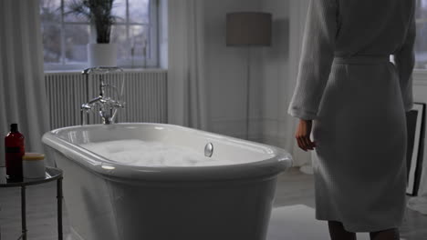 Unknown-lady-walking-bathroom-closeup.-Satisfied-woman-touching-bathtub-foam