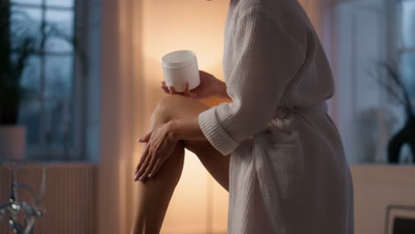 Gorgeous-woman-moisturizing-legs-at-bath-closeup.-Lady-putting-cream-at-evening