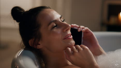 Carefree-woman-chatting-telephone-smiling-in-bathtub.-Joyful-model-laying-foam