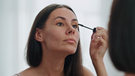 Confident-woman-applying-mascara-mirror-place.-Beautiful-model-preparing-makeup
