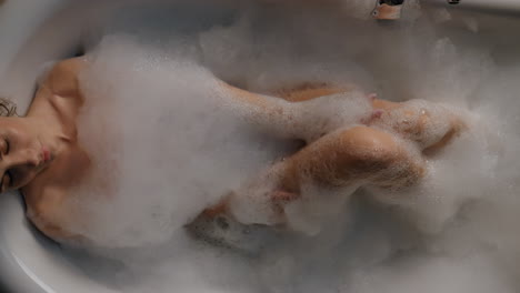 Young-lady-relaxing-foam-bathtub-top-view.-Relaxed-woman-washing-body