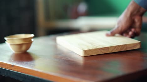 Wooden-Board-Being-Placed-On-Table-Beside-Two-Stacked-Bowls-Along-With-Salt-And-Pepper-Shakers