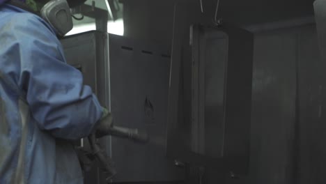 A-handheld-footage-of-a-factory-worker-wearing-a-safety-suit-while-spraying-water-on-steel-to-clean-and-cool-it-down