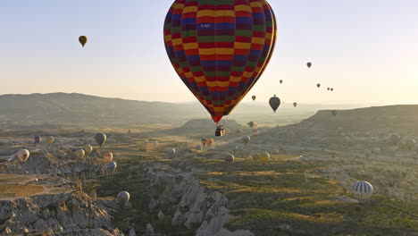 Göreme-Turkey-Aerial-v64-remarkable-landscape-of-world-heritage-site-with-unique-rock-formation,-valley,-plateau-fields-and-hot-air-balloons-in-the-sky-at-sunrise---Shot-with-Mavic-3-Cine---July-2022