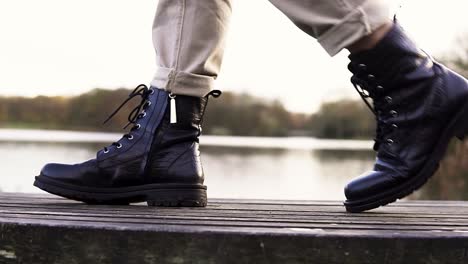 Close-up-view-of-black-leather-boots-walking-by-a-lake-in-nature-outdoor-park