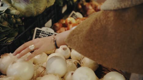 Hand-of-a-woman-choosing-an-onion-from-a-grocery-store-in-slow-motion