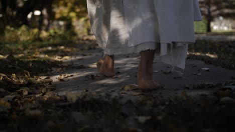 A-dramatic-slow-motion-closeup-of-Jesus'-feet-walking-down-a-sidewalk-and-on-grass-while-he-wears-a-white,-tattered-robe