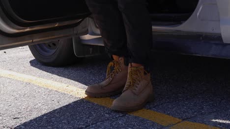 Macro-tight-shot-of-a-man's-boots-stepping-out-of-a-silver-car-on-a-sunny-day
