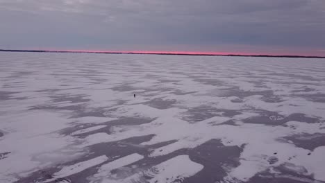 isolated-person-walking-on-frozen-lake-during-Sunrise