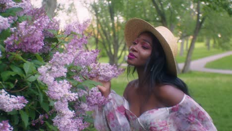 Black-lady-seductively-smells-touches-pink-Lilac-flowers-in-park,-eye-contact