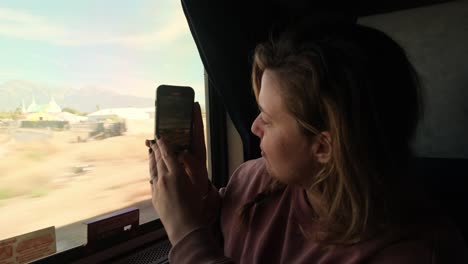 Female-Tourist-on-Train-Takes-Photos-and-Videos-on-Her-Phone-From-Window