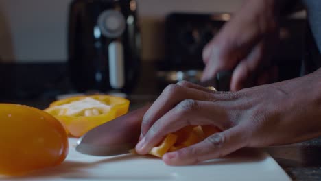 Hands-of-a-man-dicing-yellow-bell-pepper-slices-with-a-big-knife