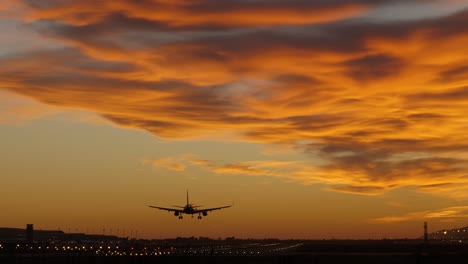 Silhouette-of-commercial-jet-landing-at-airport-during-dramatic-sunset
