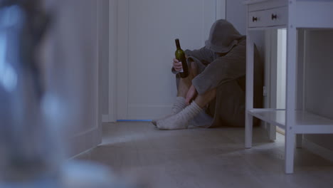 man-huddled-in-corner-of-the-room-with-bottle-of-wine