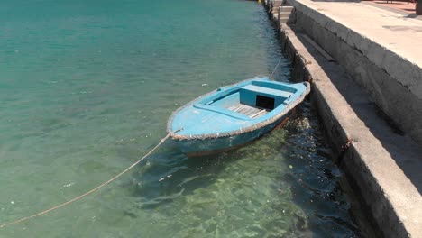A-lone-rustic-blue-wooden-rowboat-gently-bobs-in-the-warm-clear-harbor-waters,-Croatia,-Adriatic-Sea