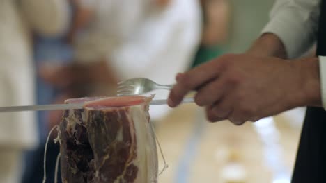 male-slicing-delicious-slice-of-dried-prosciutto-on-table,-slowmotion-closeup