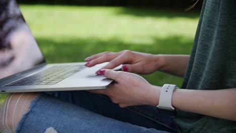 Woman-is-browsing-the-internet-on-her-laptop-while-sitting-outdoors-in-the-park