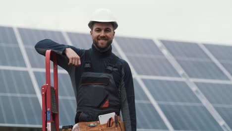 Portrait-of-a-young-man-in-a-work-uniform-with-a-toolbox-in-his-hands-on-the-background-of-a-solar-power-plant