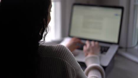 Young-woman-typing-quickly-on-a-laptop-computer-or-tablet-with-a-keyboard---view-from-behind