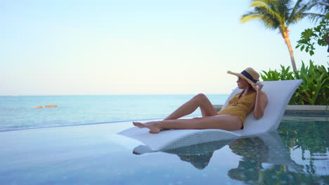 Happy-Pleased-Asian-Woman-Laying-on-Bed-in-Infinity-Pool-And-Enjoying-Alone-in-View-on-Sea-Horizon,-Static-Shot-With-Copy-Space