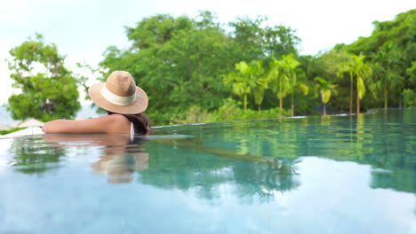 A-woman-wearing-a-hat,-relaxing-in-an-infinity-pool-at-a-luxury-hotel