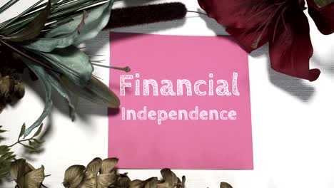 FINANCIAL-INDEPENDENCE-digitally-written-on-a-piece-of-pink-cardstock-on-a-white-canvas-backdrop-with-blue,-green-and-burgundy-floral-accents