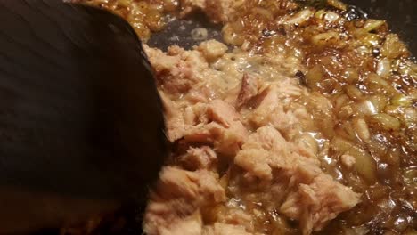 Close-up-of-tuna-fish-frying-in-a-black-frying-pan-with-white-onions-that-have-turned-golden-brown