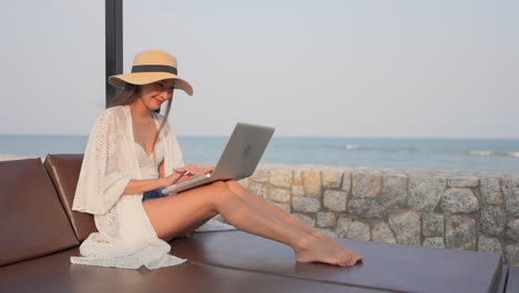 Happy-Asian-woman-using-a-computer-laptop-at-the-beach-during-travel-holidays-vacation