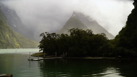 Mist-And-Clouds-Around-Mitre-Peak-In-Milford-Sound,-Fiordland,-New-Zealand-With-Small-Harbor-In-Foreground