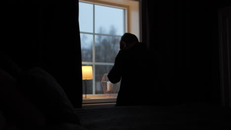 silhouetted-man-standing-by-the-window-in-despair