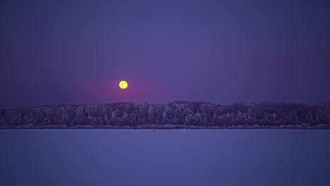 Full-moon-rising-beyond-a-frozen-lake-and-forest---dreamy-time-lapse