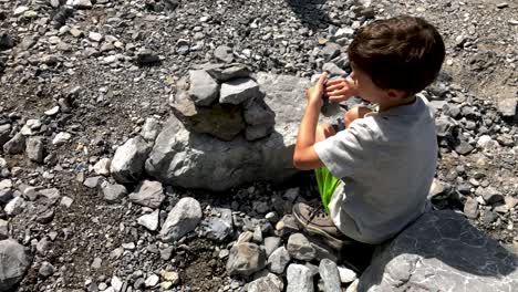 Lindo-Joven-Construyendo-Algunas-Piedras-En-Un-Río-De-Montaña-Con-La-Ayuda-De-La-Abuela