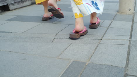 Side-angle-of-beautiful-girls-walking-in-traditional-kimono-wearing-wooden-sandles-on-a-bridge-in-Kyoto,-Japan-soft-lighting