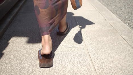 Guy-wearing-a-yukata-wearing-traditional-wooden-sandles-walking-towards-a-temple-in-Kyoto,-Japan-soft-lighting