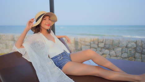 Smiling-woman-with-hat-relaxing-on-sunny-day-with-sea-in-background