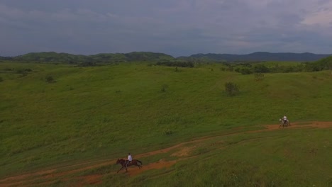 Zwei-Reiter-Galoppieren-Ihre-Pferde-Auf-Einem-Roten-Feldweg-In-Einer-Venezolanischen-Ebene,-Zeitlupe