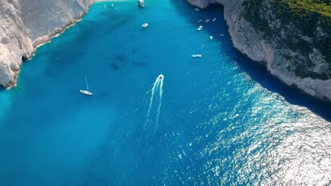 Aerial-of-tourist-boats-and-yacht-sailing-on-crystal-clear-blue-waters-surrounded-by-tall-cliffs