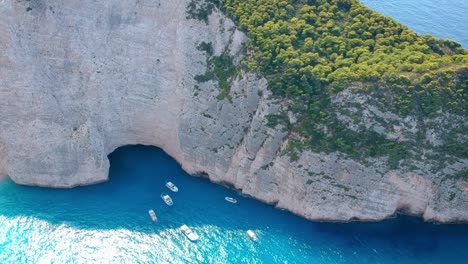 Tourist-yacht-and-boats-parked-on-deep-blue-waters-along-the-huge-cliffs-of-Zakynthos-island,-Greece