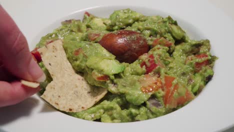 Tortilla-chip-breaks-in-hand-scooping-guacamole-from-bowl,-Closeup