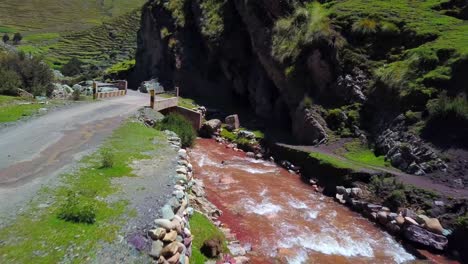Aerial,-drone-shot-of-a-road-and-a-bridge,-at-the-Pukamayu-Red-River,-on-a-sunny-day,-in-Cusco,-Peru,-South-America