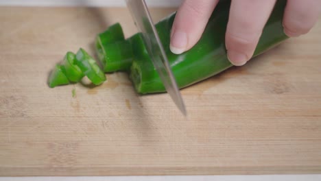 Hand-slicing-green-pepper-with-kitchen-knife-on-wooden-cutting-board,-Closeup