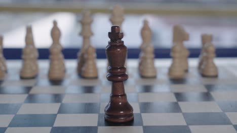 Tilt-Up,-Black-King-Chess-piece-faces-blurry-white-army-alone,-Closeup