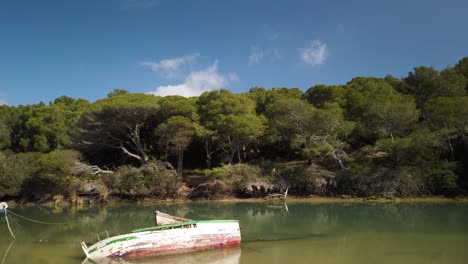 Tilt-down-reveal-of-abandoned-sunken-rowboat-in-estuary-waters,-Spain