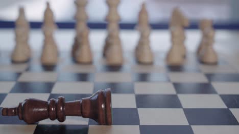 King-Chess-piece-falls-over-in-front-of-soft-focus-white-army,-Closeup