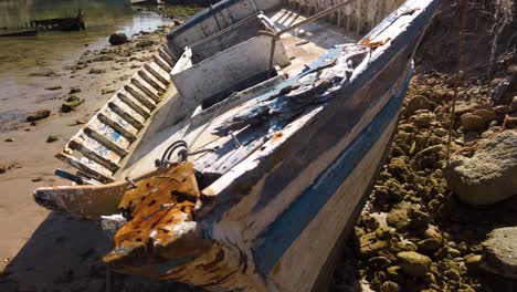 Shipwrecked-Boat-with-Blue-and-White-Stripes-on-Rocky-Beach,-Closeup-Slide-Left