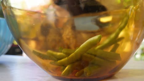 Nahaufnahme-Einer-Glasschale-Mit-Gemüse,-Während-Die-ältere-Frau-Gemüse-Im-Hintergrund-In-Zeitlupe-Schneidet