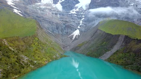 Aerial,-reverse,-drone-shot-tilting-over-the-laguna-Humantay-lake,-in-Andes-mountains,-cloudy-day,-in-Cusco-region,-Peru